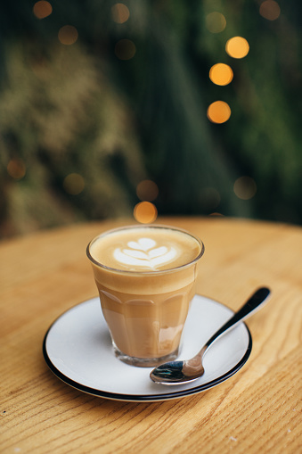 Delicious cappuccino on a Christmas background with lights and pine branches.