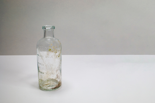 One dirty clear glass medical beaker, aged and patina on a white background.  Empty and covered with dirt and rust.
