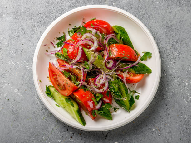 istock Vegetable salad with tomatoes and cucumbers and red onion on white plate on grey table top view 1448016862