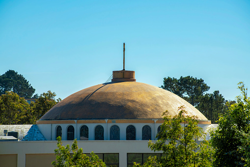 Dome on city rooftop on building or structure in the downtown neighborhood in the city streets or in an urban area of the town. Round roof with white stucco exterior and surrounding trees.