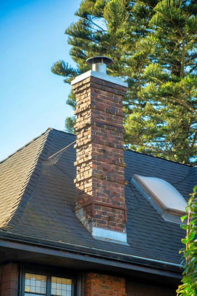 istock Brick chimney on dark tile rooftop with visible back yard towering green trees and metal top with visible window on house or home 1448019999