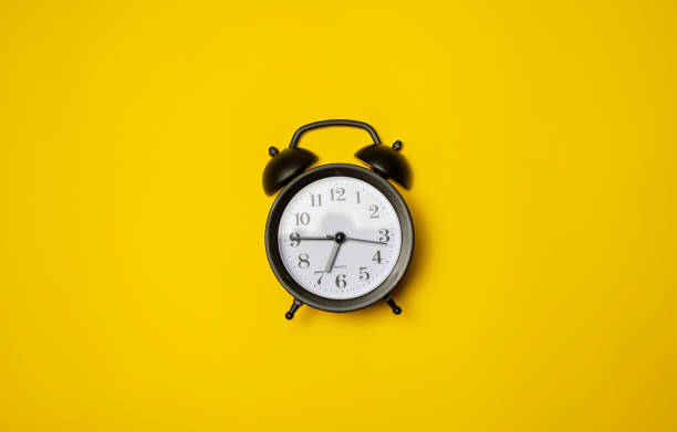istock Small black alarm clock, black numbers, set the time placed on a table. Clock on isolated yellow background. 1448024587