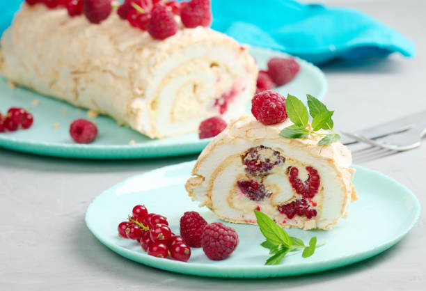 istock Baked meringue roll with red berries on a round plate, white background 1448026260