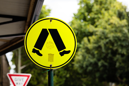 Close- up on a yellow metal street sign alerting drivers to a pedestrian crossing.