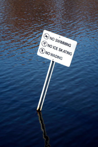 Sign askew in water warning against swimming, skating, and wading.