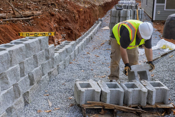 Construction site worker installing the newly constructed large block retaining wall as part of the construction of a new building stock photo