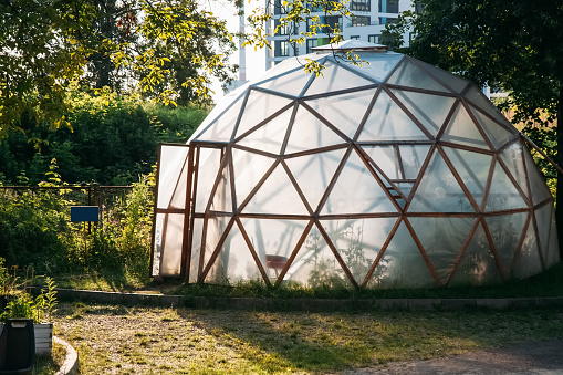 Domestic greenhouse. Cultivate farming. Natural gardening. Cupola hothouse with transparent plastic membrane geometric net frames outdoor daylight.