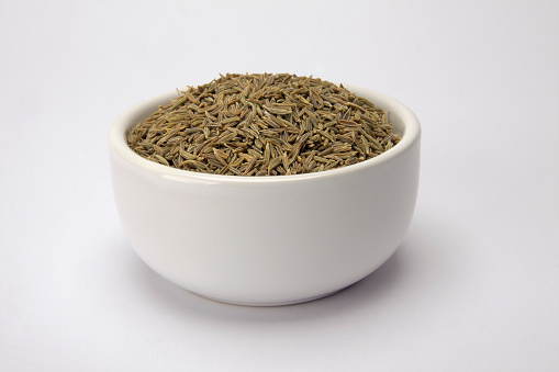 Cumin seeds in a small white bowl isolated on a white background
