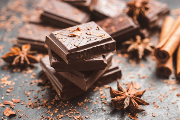 istock Dark chocolate bar pieces on dark background with grated chocolate and spices, pile chunks of broken chocolate 1448038352