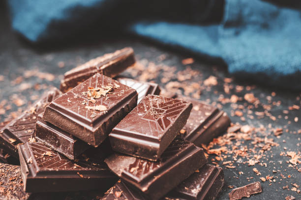 istock Dark chocolate bar pieces on dark background with grated chocolate, pile chunks of broken chocolate 1448038414