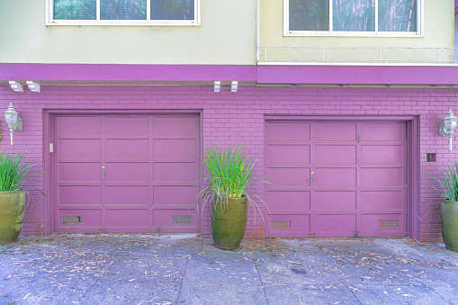 Purple garage exterior of two townhomes with potted plants near the painted bricks-San Francisco, CA. Two sectional garage doors with wall lamps on the side.