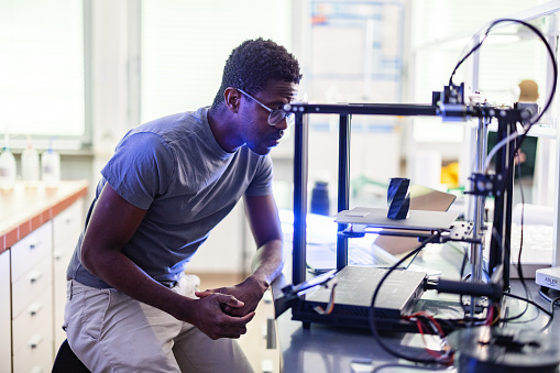 African-American designer or engineer using a 3D printer in the laboratory while studying a product prototype, and technology.
