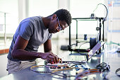 African-American Technician Repairing A 3D Printer In Laboratory
