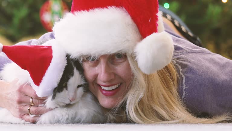 Woman and Cat in Santa Hats Snuggling Under Christmas Tree