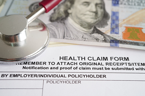 Health claim form with stethoscope and US dollar banknotes, insurance accident medical concept.