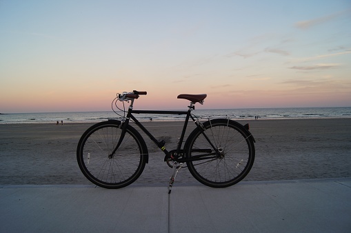 A black commuter bicycle is propped up in front of a beach and the ocean at sunset.