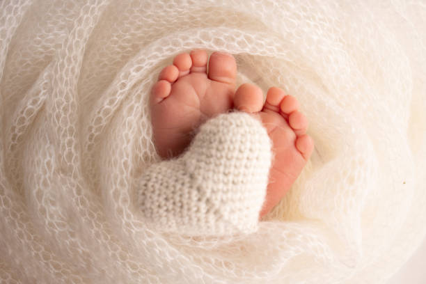 The tiny foot of a newborn baby. Soft feet of a new born in a white wool blanket. Close up of toes, heels and feet of a newborn. Knitted white heart in the legs of a baby. Macro photography. el pequeño pie de un bebé recién nacido. pies suaves de un recién nacido en una manta de lana blanca. primer plano de los dedos de los pies, los talones y los pies de un recién nacido. corazón blanco de punto en las piernas de un bebé. fotografía m