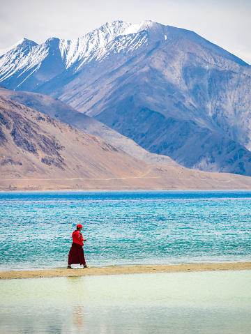 Ladakh, India - June 18, 2022 : Unidentified buddhist monk walking near beautiful Pangong lake. Vertical or portrait orientation