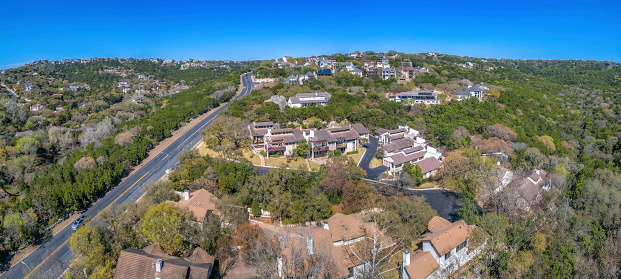 Aerial view of a residential area and highway road at Austin, Texas. There are large houses with trees outside and a view of a straight highway on the left with few vehicles passing.