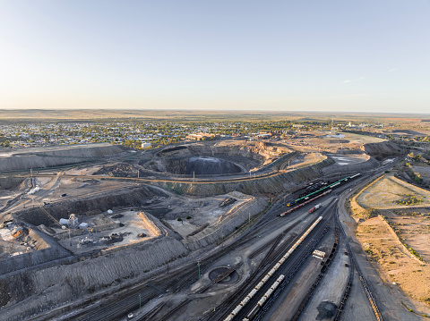 Early morning high angle aerial drone view of a big open pit silver, zinc and lead mine located within the city boundaries of Broken Hill, New South Wales, Australia. Train station in the foreground.