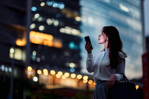 confidence young woman using smart phone on her way off work outside office building at night