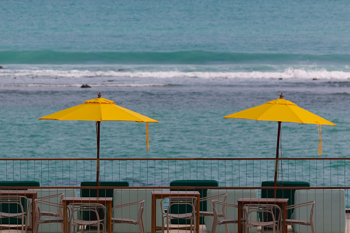 Two yellow beach umbrellas and a dining table set against the backdrop of the sea.