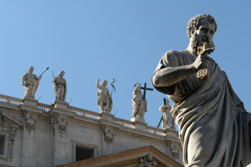 Statue in foreground, Vatican basilica in background. Space for copy on bright blue sky.