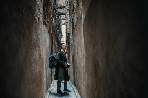 Asian Chinese male tourist looking up at narrow alley in the old medina of Fez, Morocco