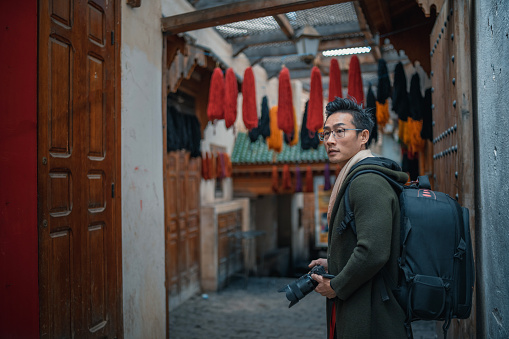Asian Chinese male tourist admiring in souk market in  Coloured dyed yarn hanging dried on the streets of Fez, Morocco