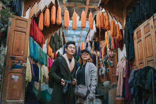 Asian Chinese tourist couple walking in alley of souk market in  Coloured dyed yarn hanging dried on the streets of Fez, Morocco