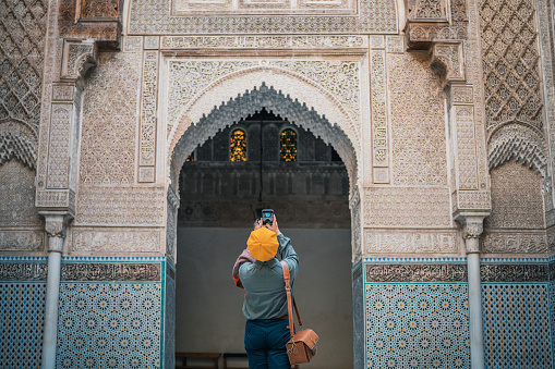 Asian Chinese female tourist photographing and admiring Fez Mosque Bou Inania Madressa