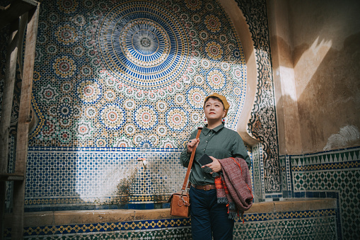 Asian Chinese female tourist resting at public drinking fountain in the Old City of Fez, Fes, Morocco