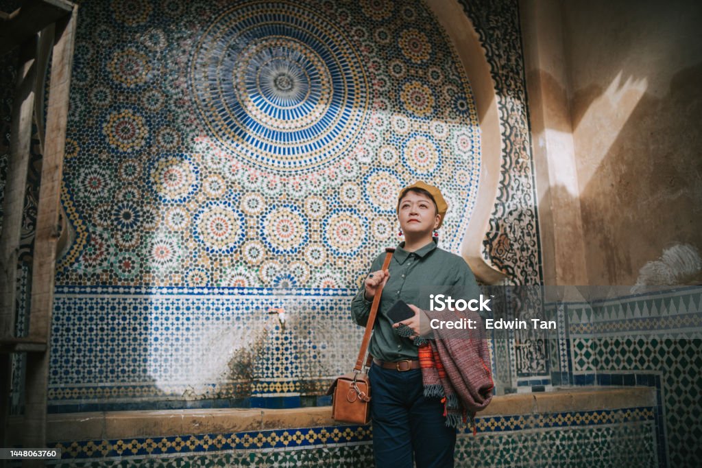 Asian Chinese female tourist resting at public drinking fountain in the Old City of Fez, Fes, Morocco Mosaic Stock Photo