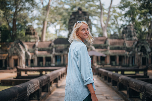 A young adult  woman walks towards one of the entrances to the Ta Prohm temple, in the Angkor temple complex in Cambodia.