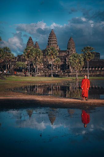 Siem Reap, Cambodia - November 14, 2022. Buddhist monk in front of Angkor Wat reflecting  in the lake.
