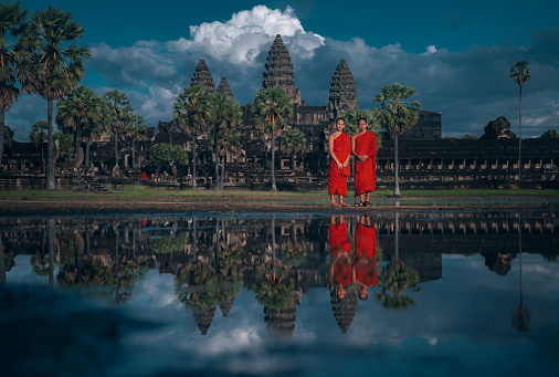Siem Reap, Cambodia - November 14, 2022. Two monks in front of Angkor Wat reflecting  in the lake.