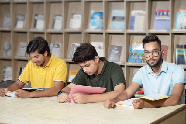 istock Young indian student boys reading books and studying in college library with bookshelf behind. 1448069452