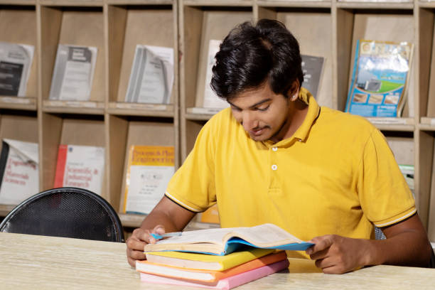 istock Young indian student boy reading book studying in college library with bookshelf behind. working on assignment or project. 1448069977