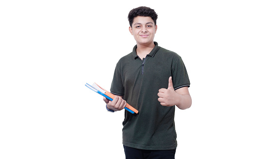 Portrait of happy indian teenager college or school boy holding books do thumbs up isolated on white background.