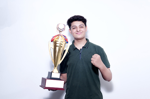 Confident indian teenager college or school boy holding golden victory trophy cup in hand isolated on white background. winner.