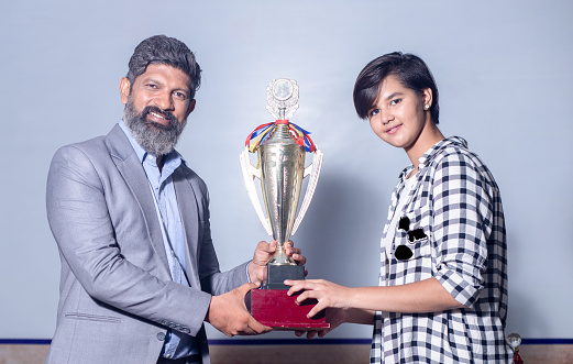 Indian man school teacher give victory golden trophy cup to girl student, Female receive winning prize.