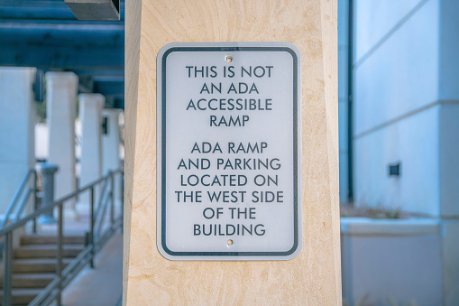 Austin, Texas- Sign on a pillar with This is not an ADA accessible ramp. Close-up of a sign with a message of the location of the ADA ramp and parking against the background of pillars and stairs.