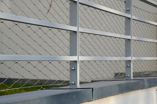 stainless steel railing on the concrete wall of the roof parking lot. anchored screws to the foot of the attic. sheet metal drains rainwater. steel wire mesh against children falling, loop