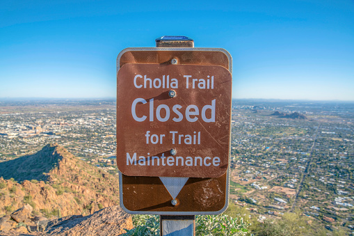 Phoenix, Arizona- Cholla Trail Closed for Trail Maintenance on a signage at Camelback Mountain. Close-up of a signage against the landscape view below against the blue skyline.