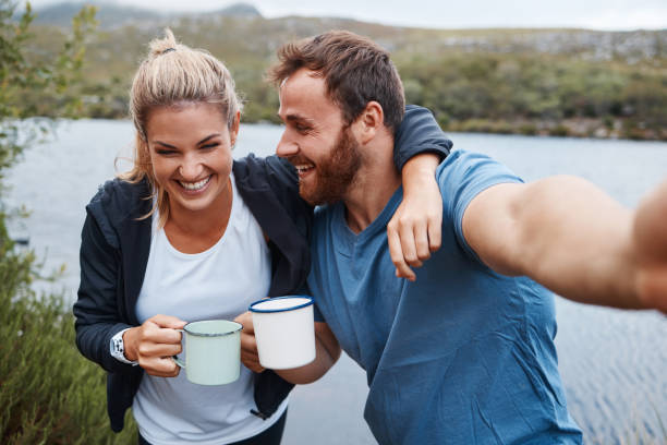 naturaleza, camping y selfie pareja con bebida de café feliz con vacaciones de aventura en el lago de méxico. vacaciones, relax y felicidad de las personas que disfrutan de bebidas calientes en la fotografía de la taza camper. - couple outdoors coffee friendship fotografías e imágenes de stock