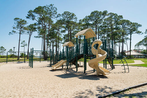Destin, Florida- Playground on a sand with slides, monkey bars, and swings. Playground near the tall trees and grass land field at the background.