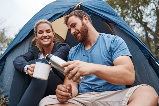 Camping, coffee and love with a couple in a tent, drinking from a flask while hiking together in nature. Tea, summer and relax with a man and woman in the natural mountains for bonding or adventure