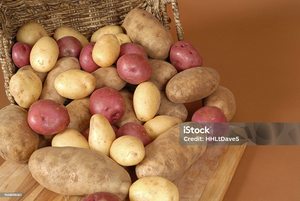 Brun roux, rouge et blanc de pommes de terre débordant d'un panier - Photo de Blanc libre de droits