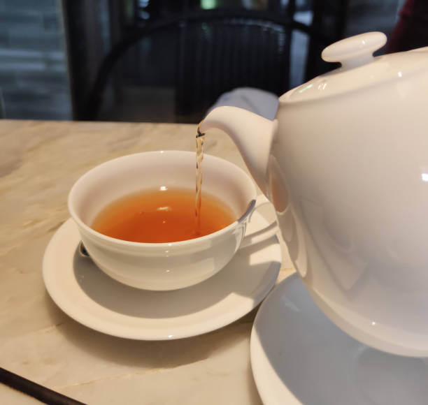 istock Tea party time. Hostess pours tea into white ceramic cups on festive table 1448081524
