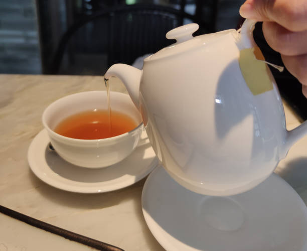 istock Tea party time. Hostess pours tea into white ceramic cups on festive table 1448081527